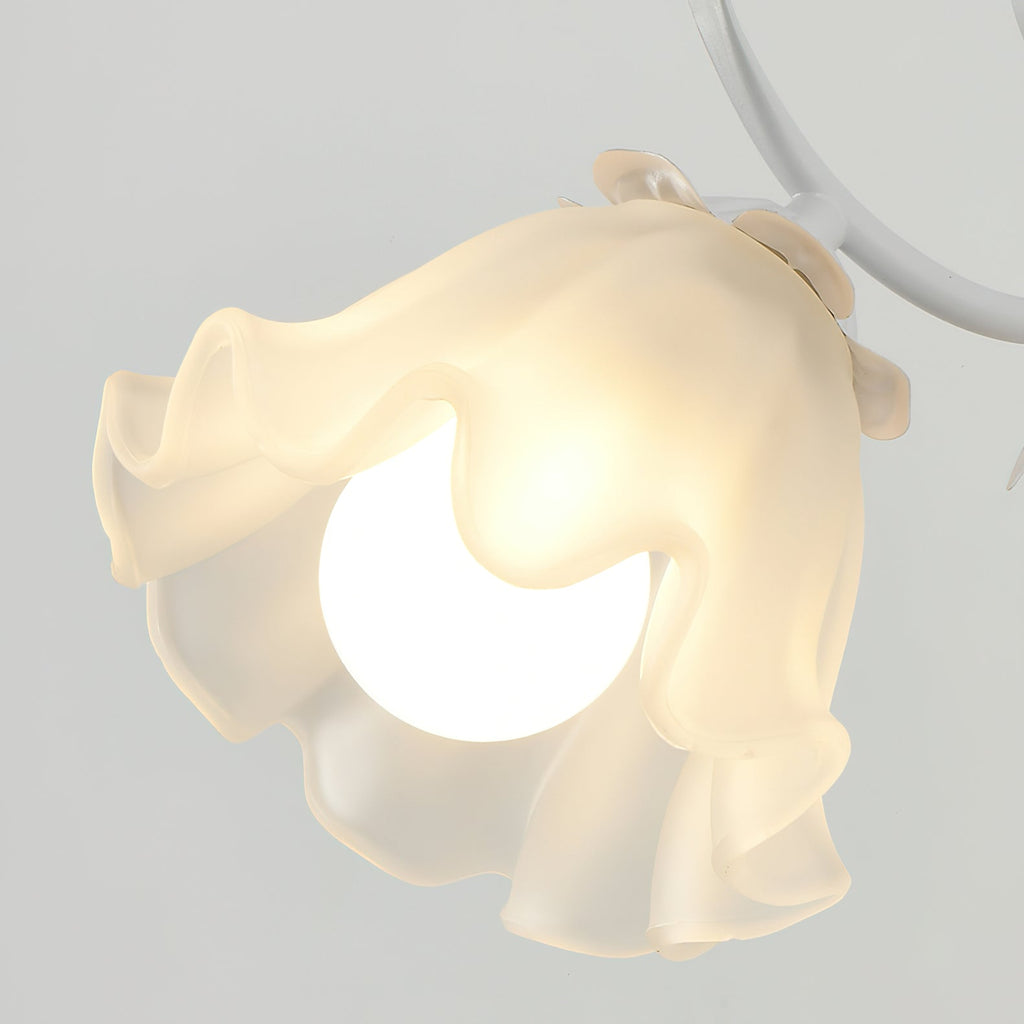 Close view of the ruffled frosted glass flower shade and bulb on a white-armed Clérachic wall light.
