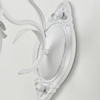 Close view of the carved oval backplate and curved white arm of this Clérachic wall light.