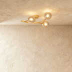 Clérachic three-globe ceiling light on a curved gold arm, smoked glass globes lit warm against limewash plaster.