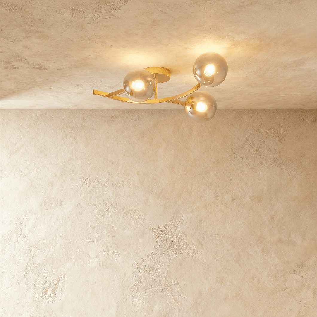 Clérachic three-globe ceiling light on a curved gold arm, smoked glass globes lit warm against limewash plaster.