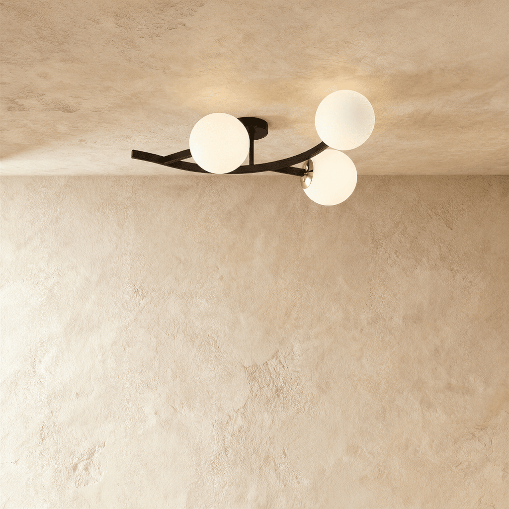 Clérachic three-globe ceiling light on a curved black arm with opal white glass globes, lit against plaster.