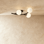 Clérachic three-globe ceiling light on a curved black arm with opal white glass globes, lit against plaster.