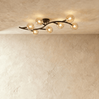 Clérachic seven-globe ceiling light on a sweeping black arm with amber-tinted glass globes, lit on plaster.