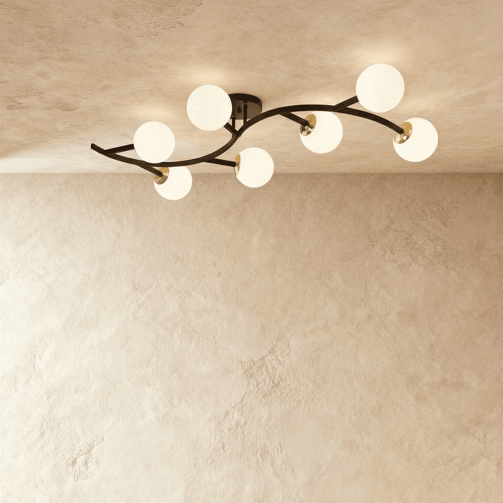 Clérachic seven-globe ceiling light with a sweeping black arm, brass joints and opal white glass globes, lit.