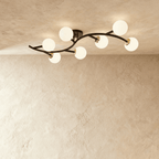 Clérachic seven-globe ceiling light with a sweeping black arm, brass joints and opal white glass globes, lit.