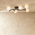 Clérachic five-globe ceiling light with a sweeping black arm, nickel-toned joints and opal white globes, lit.