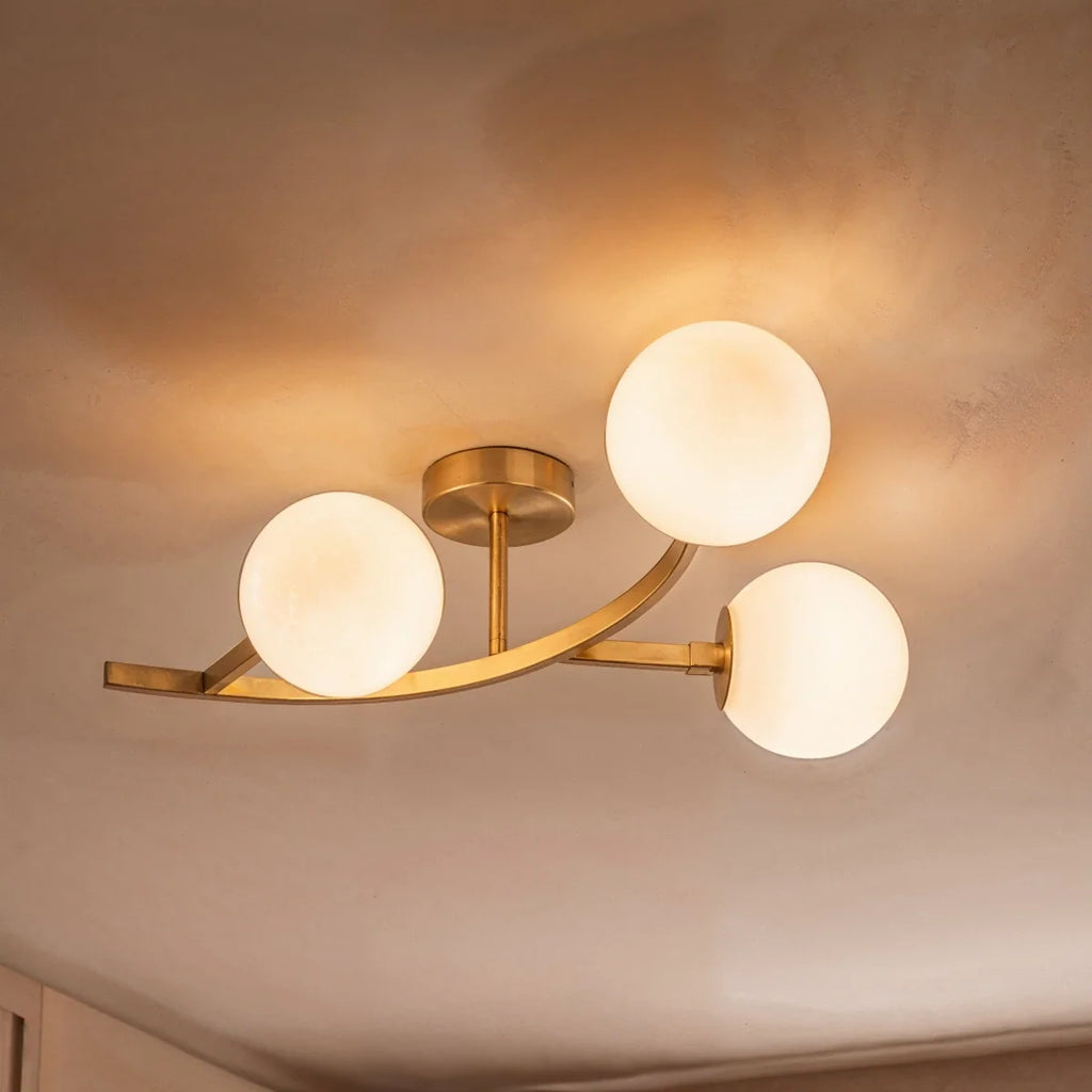 Close view of a Clérachic three-globe ceiling light in brushed gold with opal white glass, glowing on the ceiling.