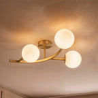 Close view of a Clérachic three-globe ceiling light in brushed gold with opal white glass, glowing on the ceiling.