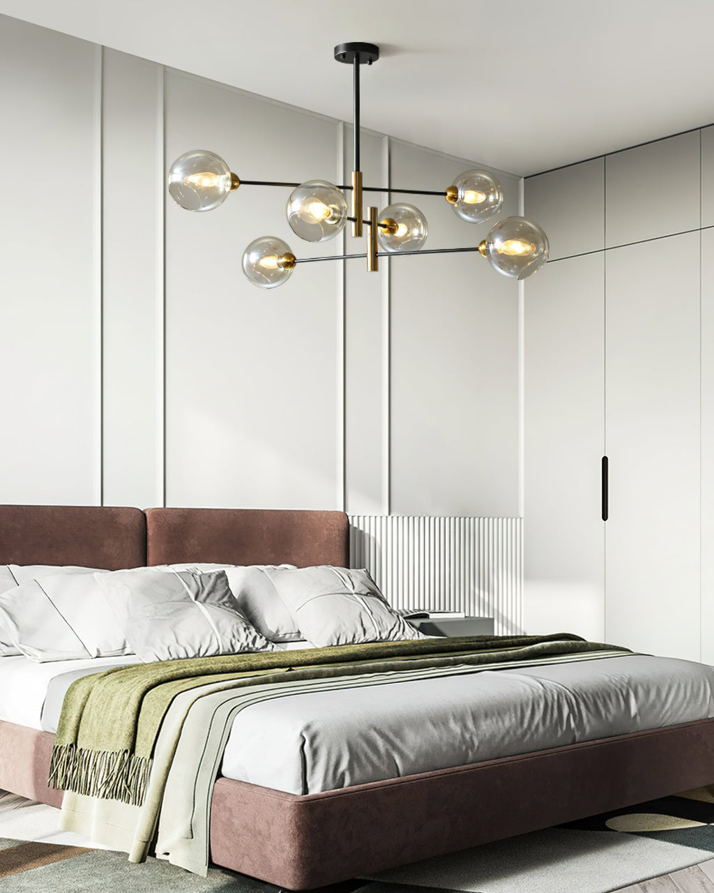 Clérachic chandelier with globe shades above a bed with a mauve headboard, a green throw and white linen, in a pale panelled room.
