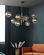 Clérachic chandelier with lit amber globes against a dark teal wall, with dried grasses in a vase and an orange sofa below.