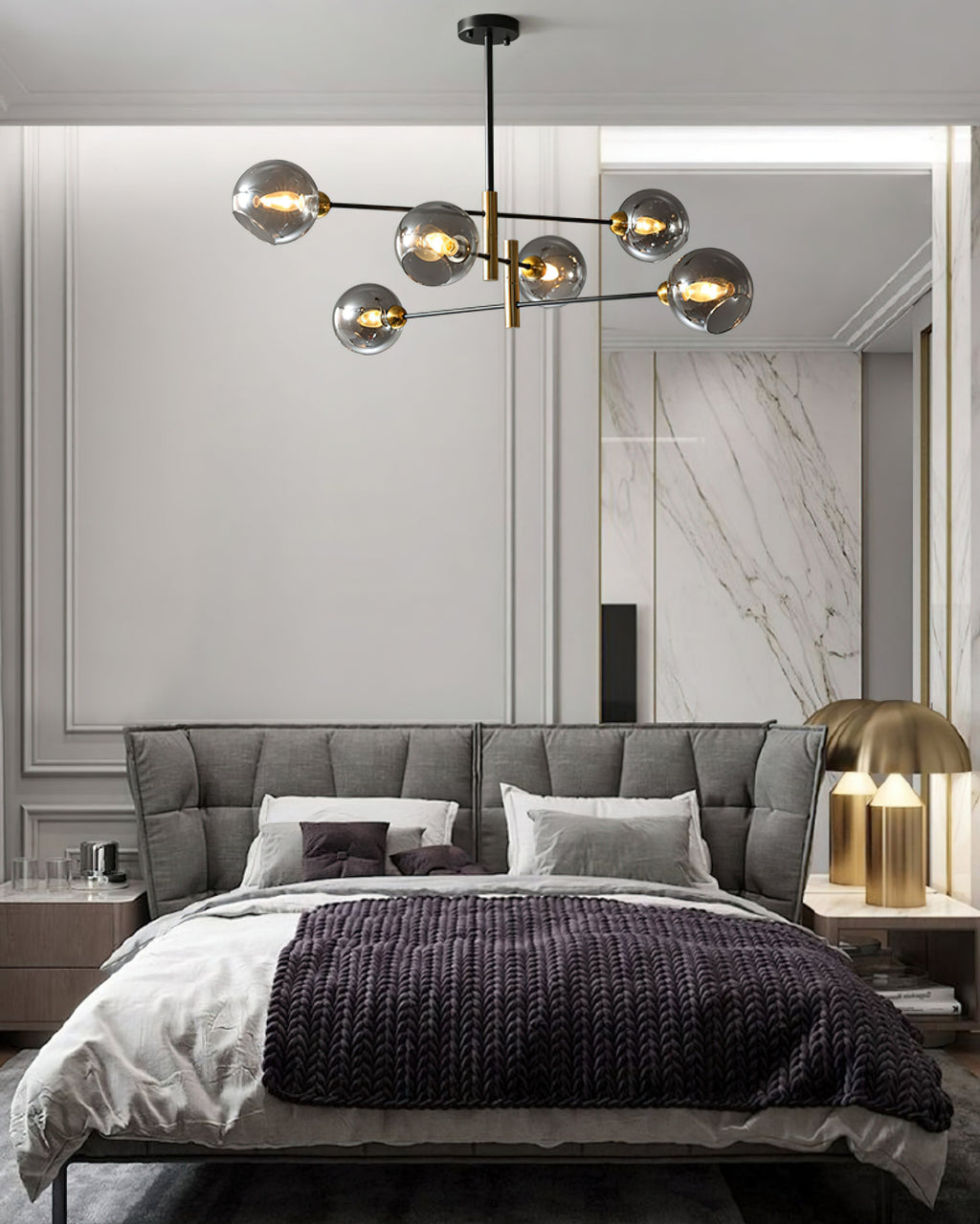 Clérachic chandelier with smoky globes above a grey tufted bed with a plum throw, in front of a marble feature wall.