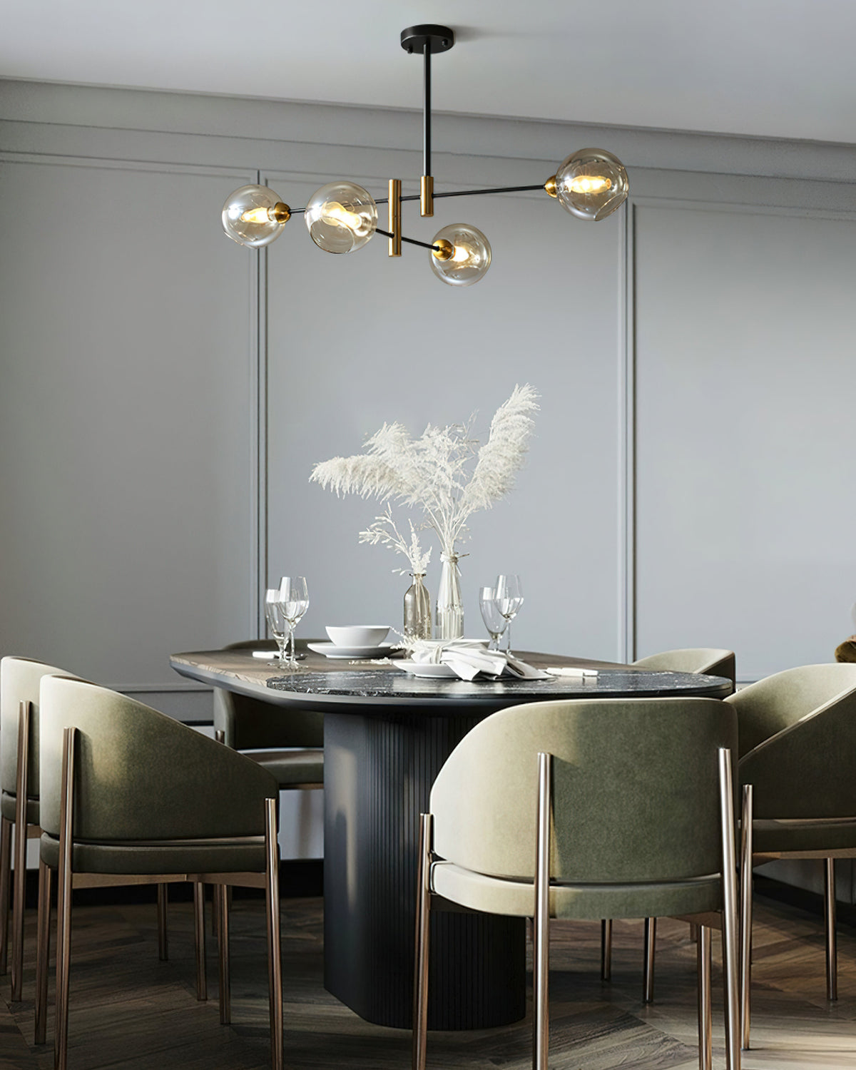 Clérachic chandelier with small amber globes above an oval dining table with olive green chairs and a vase of pampas grass.