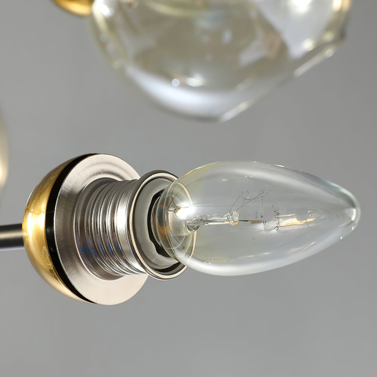 Close view of a clear bulb in a brass-toned socket on this Clérachic chandelier, with a glass globe shade above it.