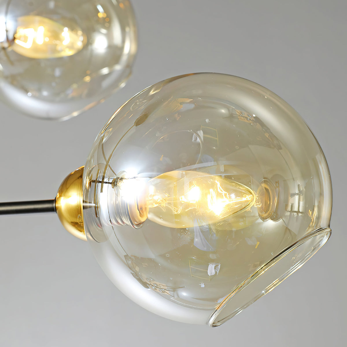 Close view of one amber glass globe on this Clérachic chandelier, with the lit bulb visible through the open side of the shade.