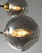 Close view of two smoky grey glass globes on this Clérachic chandelier, each with a lit bulb and a brass cap.