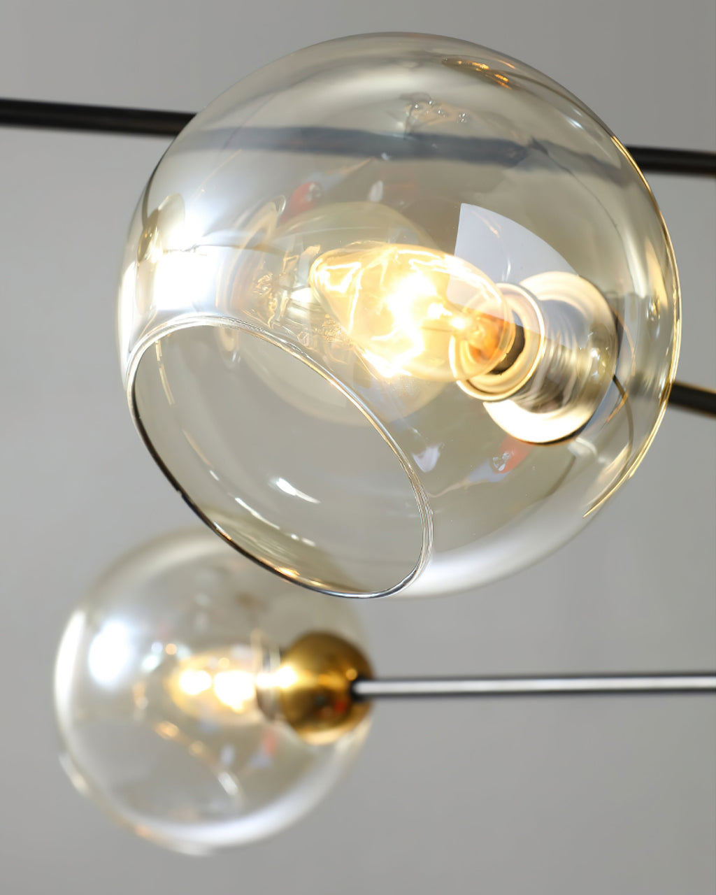Close view of an amber glass globe with a lit filament bulb, seen from below, on a black arm of this Clérachic chandelier.