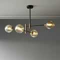 Four-head Clérachic chandelier with amber globes lit on staggered black arms, below a grey ceiling with a plain cornice.