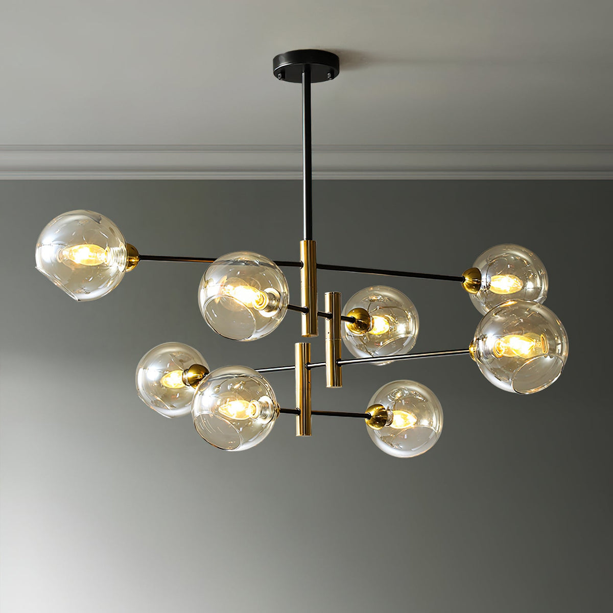 Eight-head Clérachic chandelier with amber globes, all lit, hanging from a black ceiling plate against a grey wall.