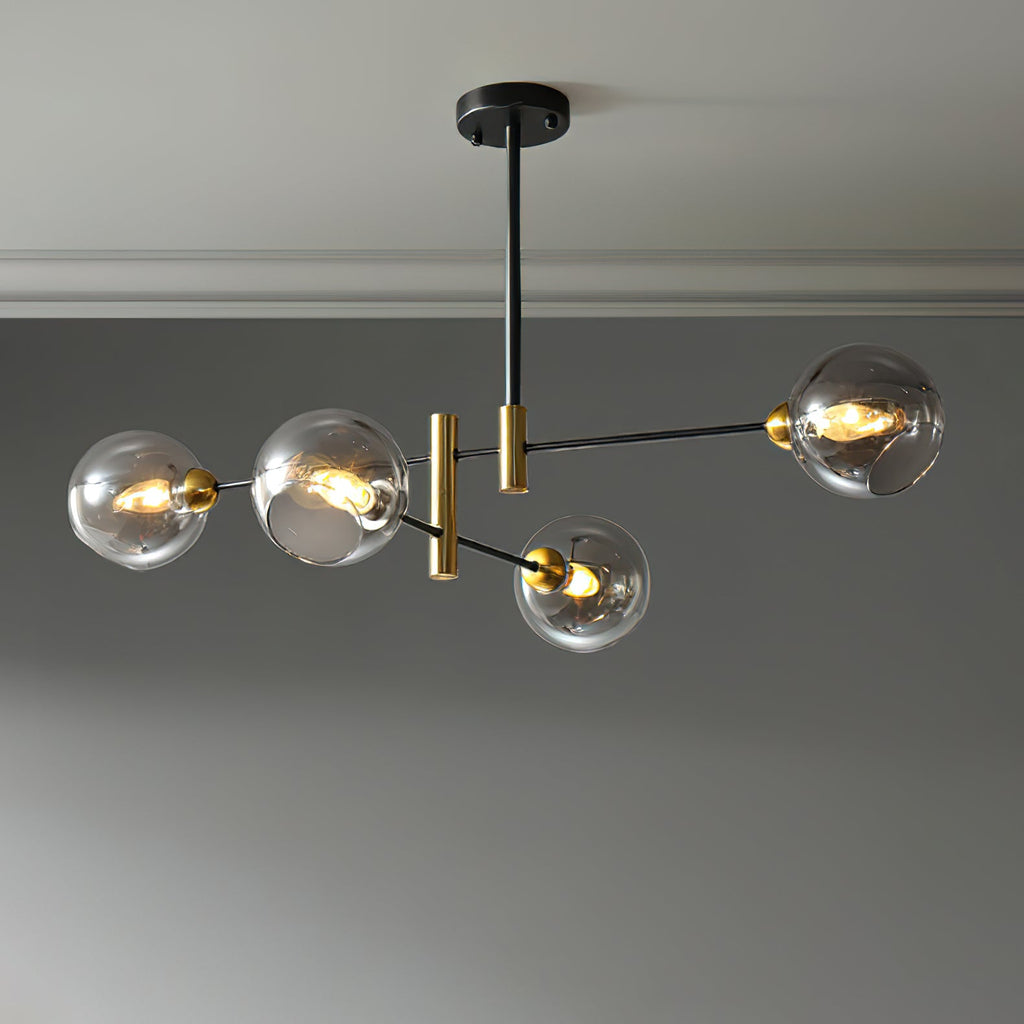 Four-head Clérachic chandelier with smoky grey globes, lit on staggered black arms against a grey wall.