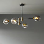 Four-head Clérachic chandelier with smoky grey globes, lit on staggered black arms against a grey wall.
