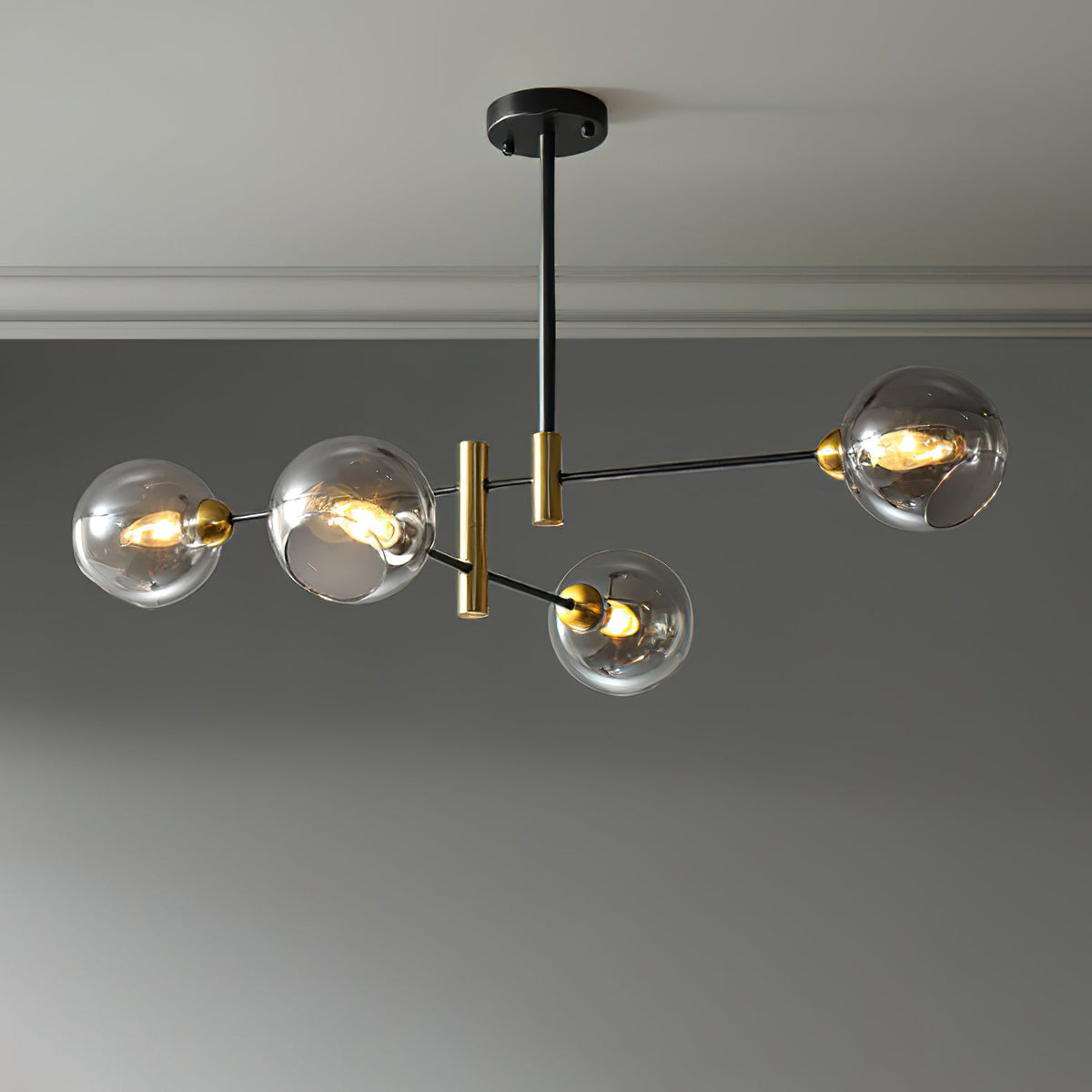 Four-head Clérachic chandelier with smoky grey globes, lit on staggered black arms against a grey wall.