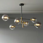 Six-head Clérachic chandelier with smoky grey globes lit on black arms and brass-toned stems, against a grey wall.