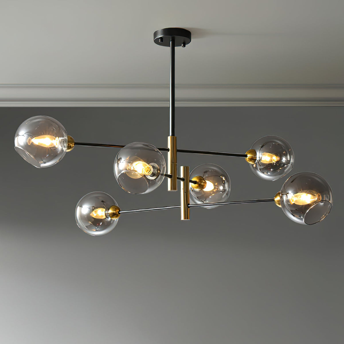 Six-head Clérachic chandelier with smoky grey globes lit on black arms and brass-toned stems, against a grey wall.