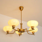 Clérachic five-head copper chandelier lit warm, its five opal globes glowing against a beige evening ceiling.