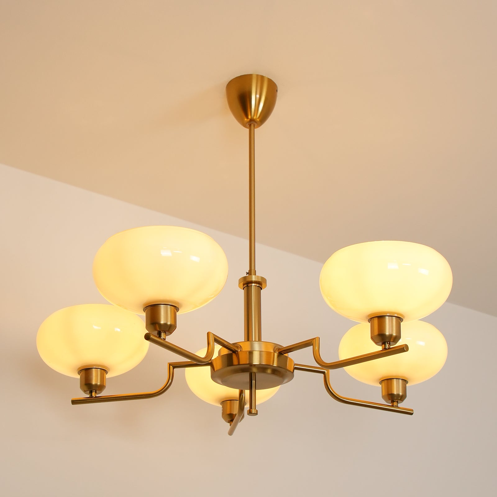 Clérachic five-head copper chandelier lit warm, its five opal globes glowing against a beige evening ceiling.