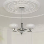 The Clérachic three-head chrome chandelier hangs below a moulded ceiling rose in a panelled white room.