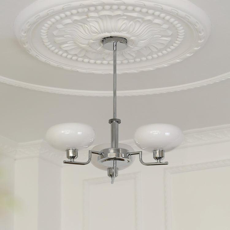 The Clérachic three-head chrome chandelier hangs below a moulded ceiling rose in a panelled white room.