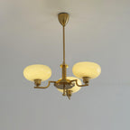 Clérachic three-head copper chandelier lit warm, cream glass globes glowing against a grey moulded wall.