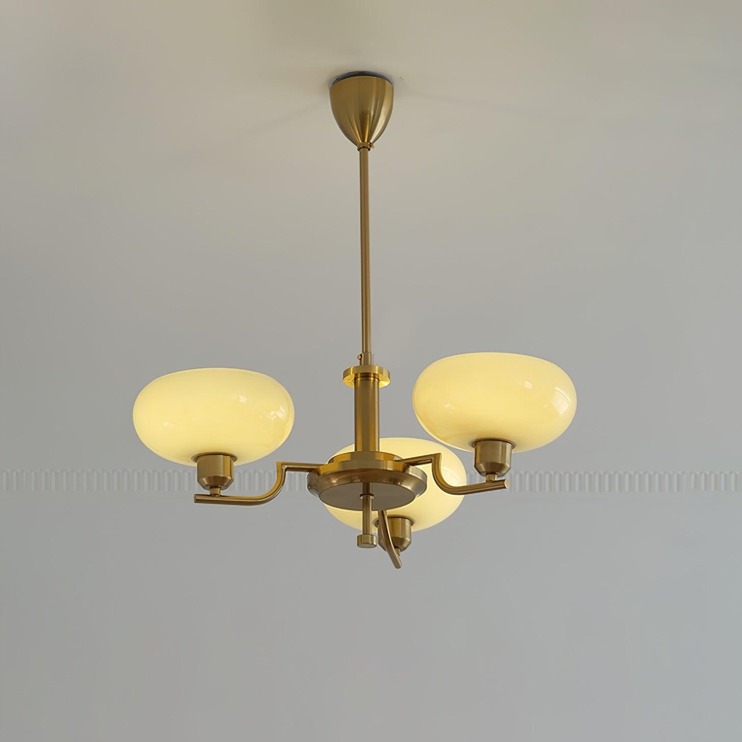 Clérachic three-head copper chandelier lit warm, cream glass globes glowing against a grey moulded wall.