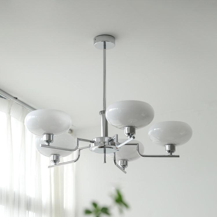 Clérachic five-head chrome chandelier with white glass globes, hung beside a sheer-curtained window.