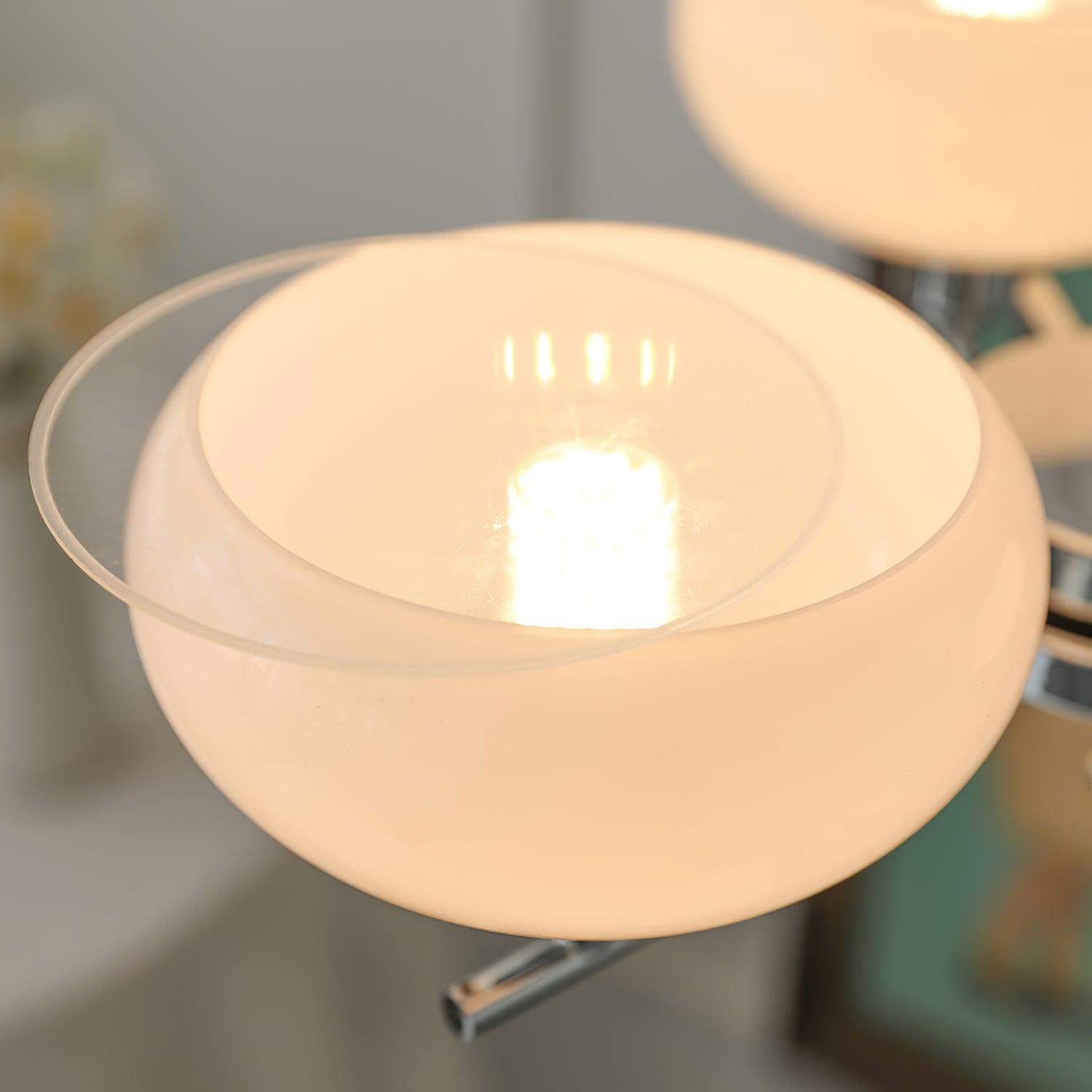 Close-up of a Clérachic glass globe on a chrome arm, warm bulb glow visible through the lit opal shade.