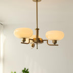 Clérachic three-head copper chandelier with cream glass globes lit warm, hung near a green houseplant.