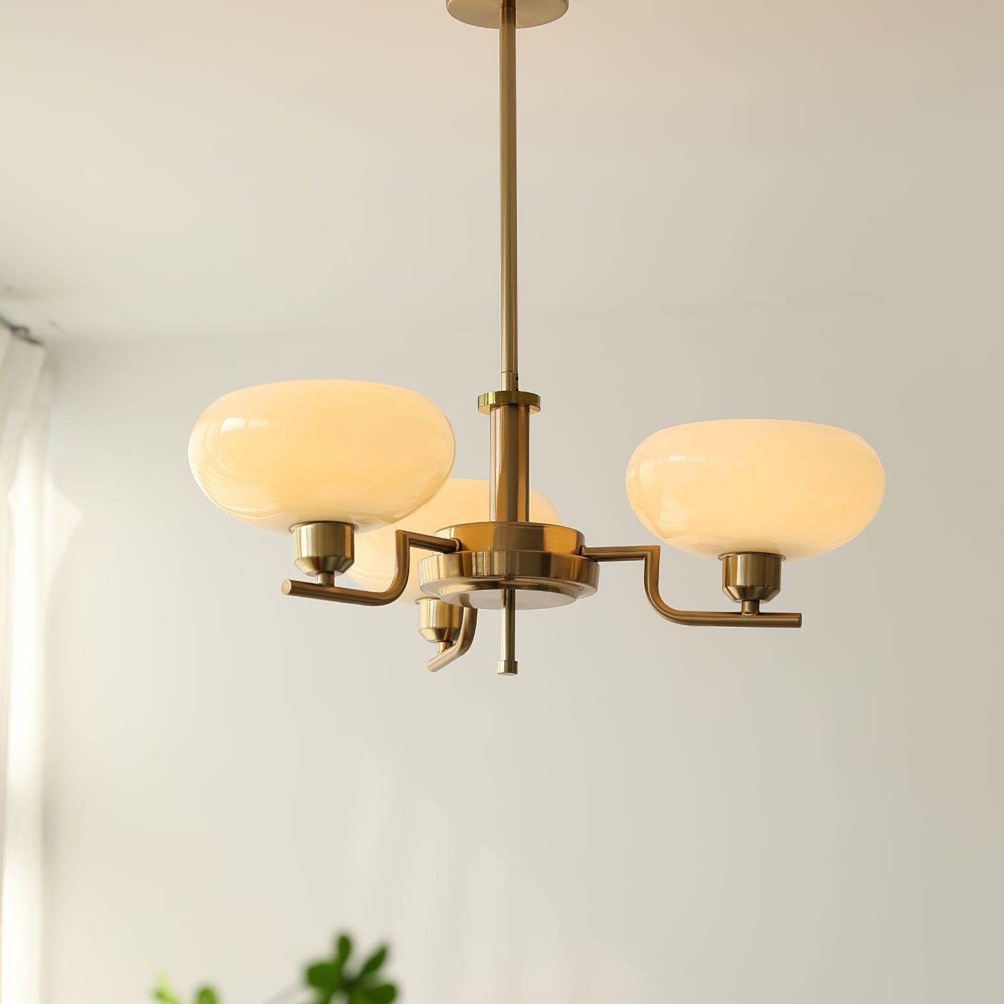 Clérachic three-head copper chandelier with cream glass globes lit warm, hung near a green houseplant.