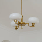 Clérachic three-head copper chandelier with cranked arms and white globes, hung near a moulded ceiling corner.