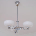 Clérachic three-head chrome chandelier with milk-glass globes, low-angle view beside crown moulding.