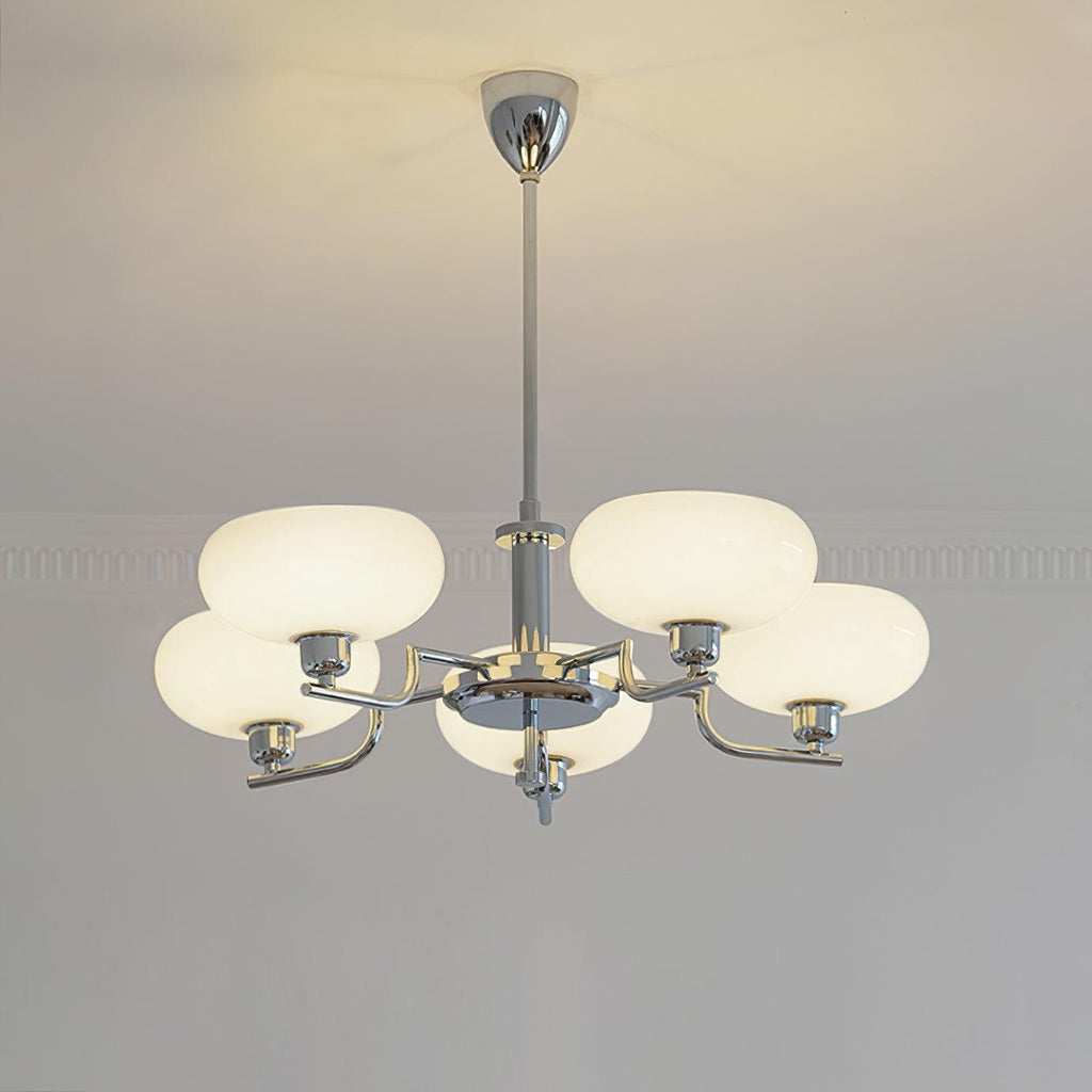 Clérachic five-head chrome chandelier lit warm, five flattened globes glowing above a moulded wall.