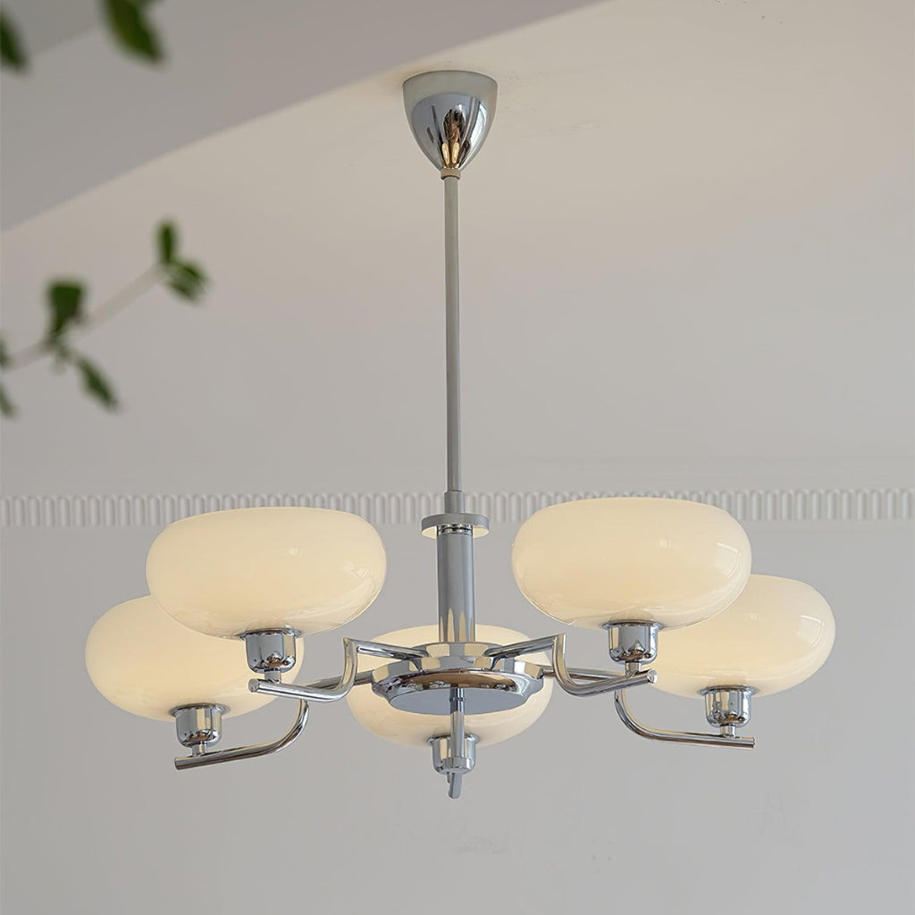 Clérachic five-head chrome chandelier with cream globes glowing, green leaves at the top of the frame.