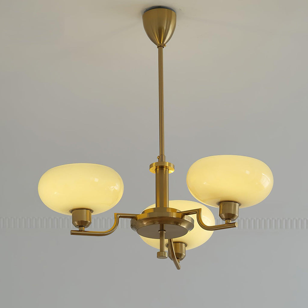 Clérachic three-head copper chandelier lit, three warm opal globes glowing against a moulded pale wall.