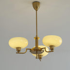 Clérachic three-head copper chandelier lit, three warm opal globes glowing against a moulded pale wall.