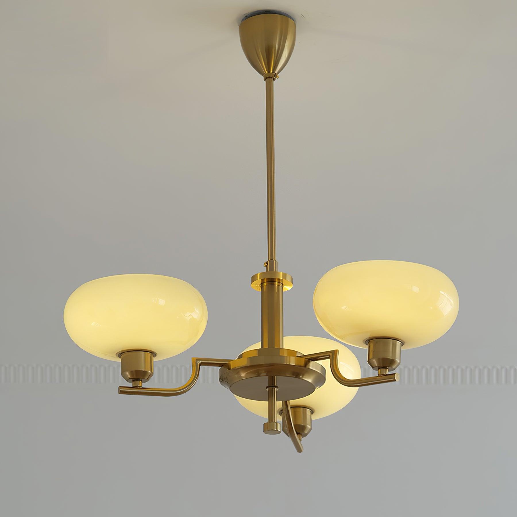 Clérachic three-head copper chandelier lit, three warm opal globes glowing against a moulded pale wall.