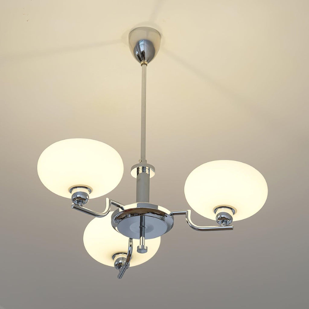 Clérachic three-head chrome chandelier lit, three frosted white globes glowing on a plain white ceiling.