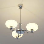 Clérachic three-head chrome chandelier lit, three frosted white globes glowing on a plain white ceiling.