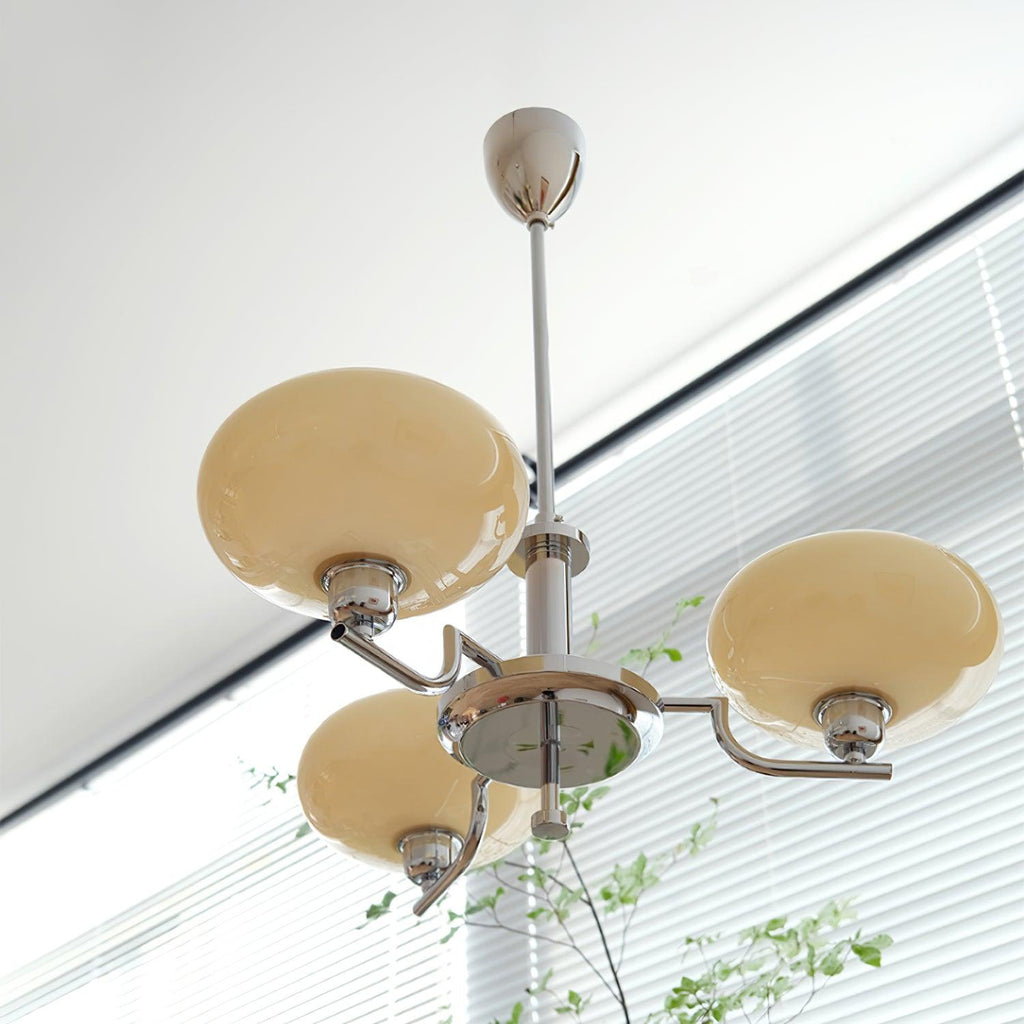 Clérachic three-head chrome chandelier with cream globes, hung beside a window with horizontal blinds.