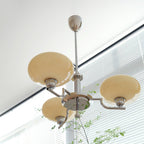 Clérachic three-head chrome chandelier with cream globes, hung beside a window with horizontal blinds.