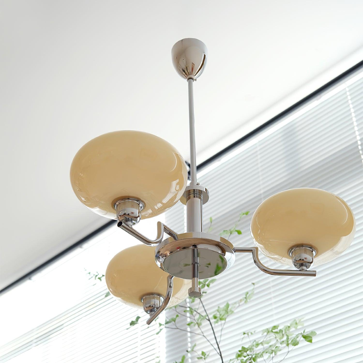 Clérachic three-head chrome chandelier with cream globes, hung beside a window with horizontal blinds.