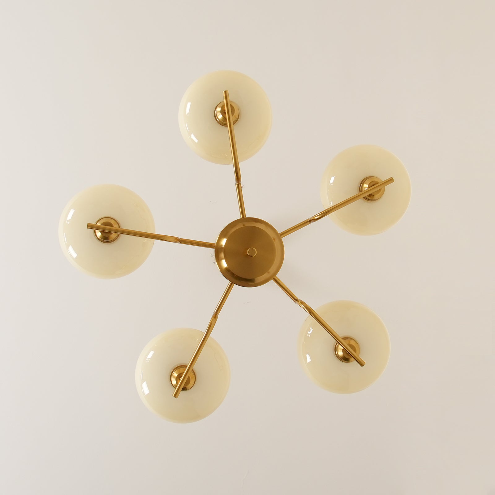 Clérachic five-head copper chandelier from directly below, five unlit white globes in a star pattern.